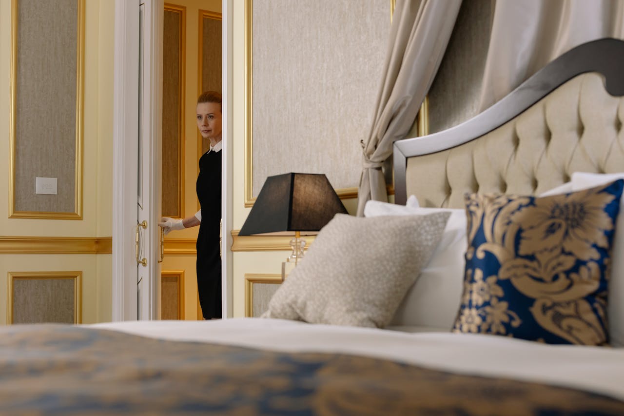 Luxurious hotel room setting with housekeeper entering the room, showcasing elegant design and decor.